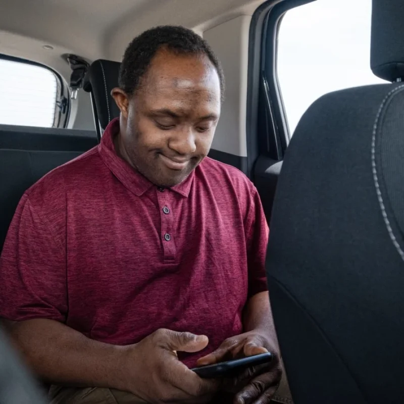 Disabled man with down syndrome sitting in back of car using mobile phone